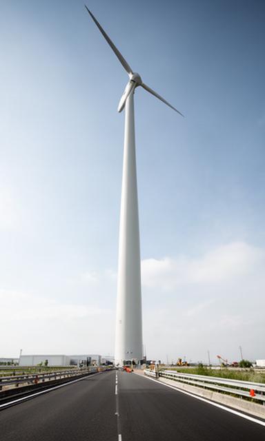 Torre de aerogenerador elevándose junto a una carretera de acceso industrial