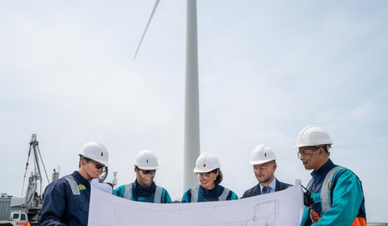 Equipo técnico revisando planos junto a una torre eólica en una instalación industrial
